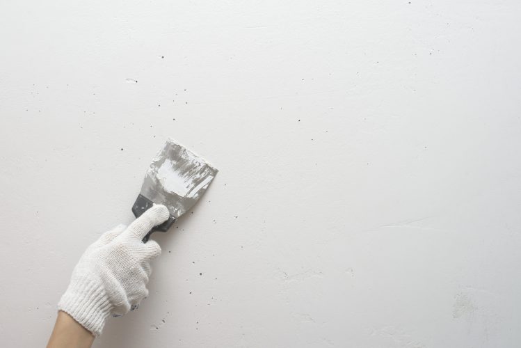Working tool, spatula in hand against the background of a white wall, work plasterer. Putty walls with their own hands.